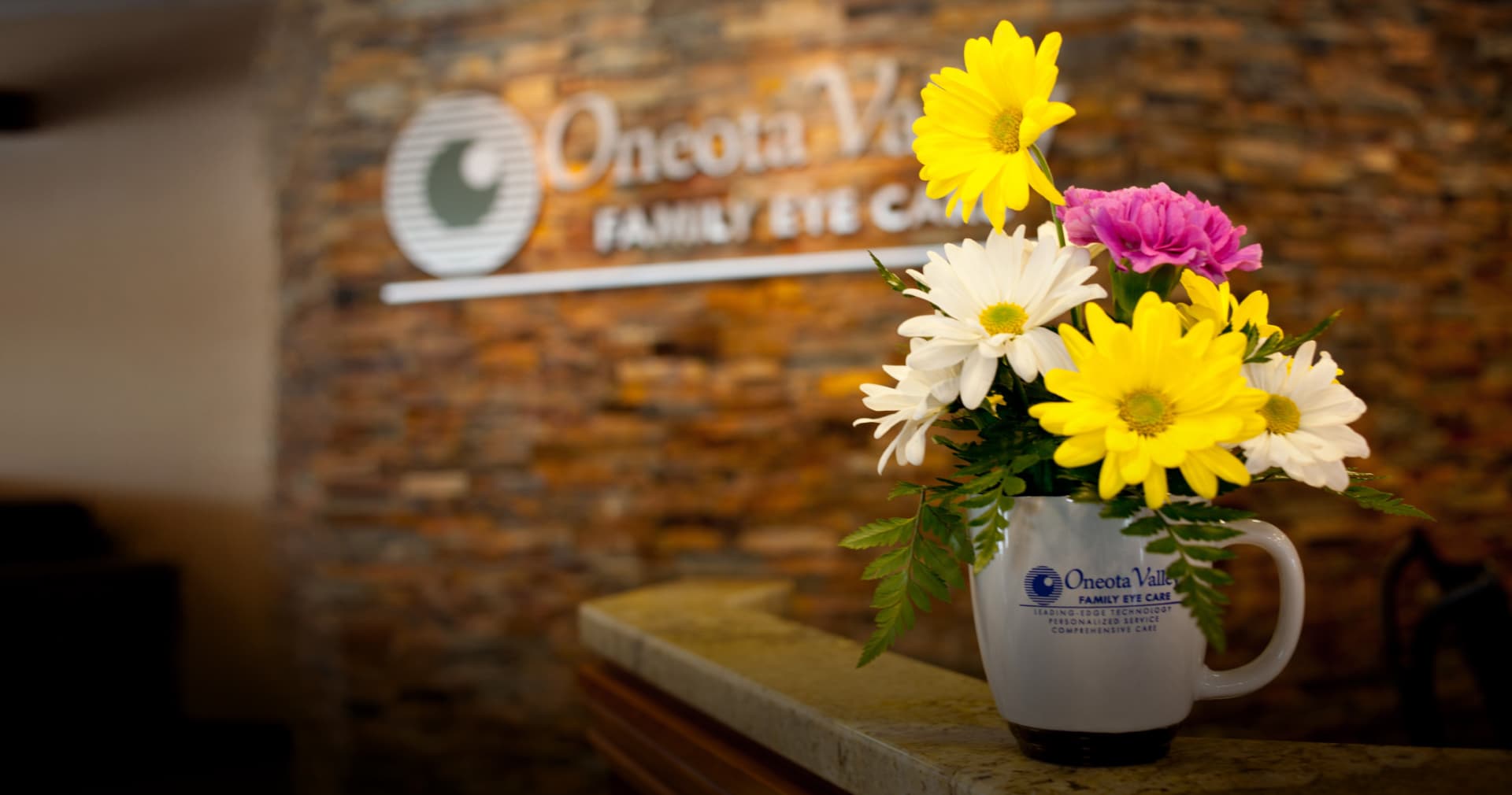 Oneota Valley Family Eye Care reception: the practice sign on a stone wall and flowers in an Oneota Valley mug